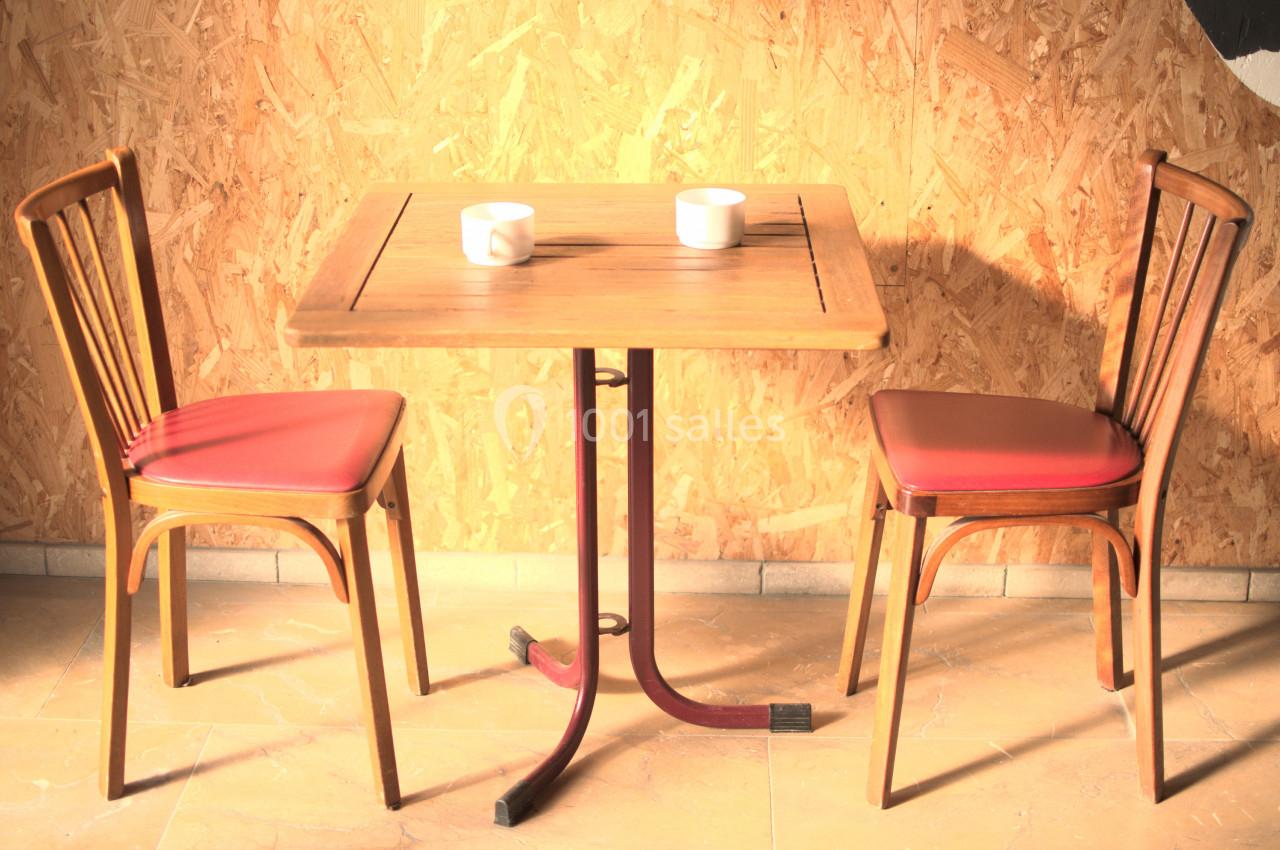 Deux chaises en bois avec assise rouge entourent une table en bois, deux tasses blanches posées dessus.
