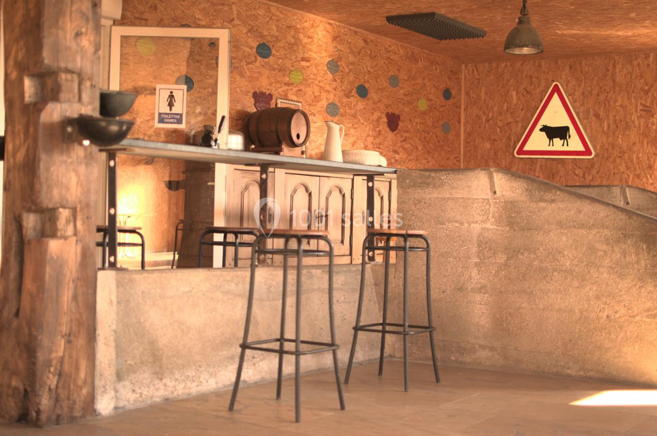 Intérieur rustique avec un bar en bois, tabourets hauts, mur en bois décoré et panneau de signalisation avec une vache.