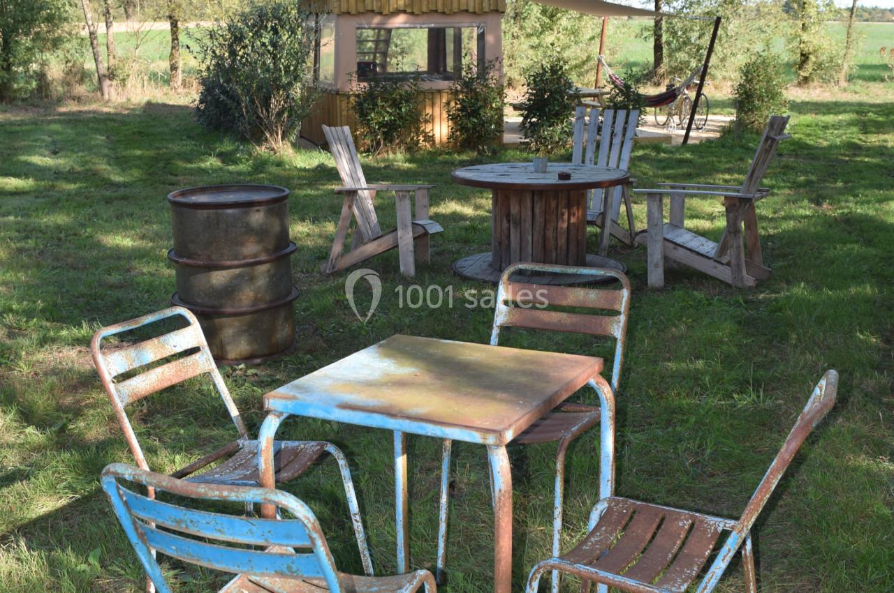 Mobilier de jardin en métal et bois disposé sur une pelouse, avec une cabane en arrière-plan entourée d'arbres.