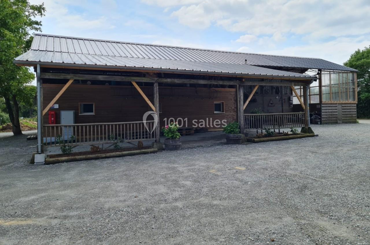 Bâtiment en bois avec toit en tôle, terrasse couverte et jardinières, situé sur un sol gravillonné.