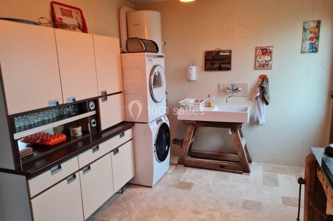 Buanderie avec lave-linge, sèche-linge empilés, évier sur pied en bois, meubles de rangement et décoration murale.