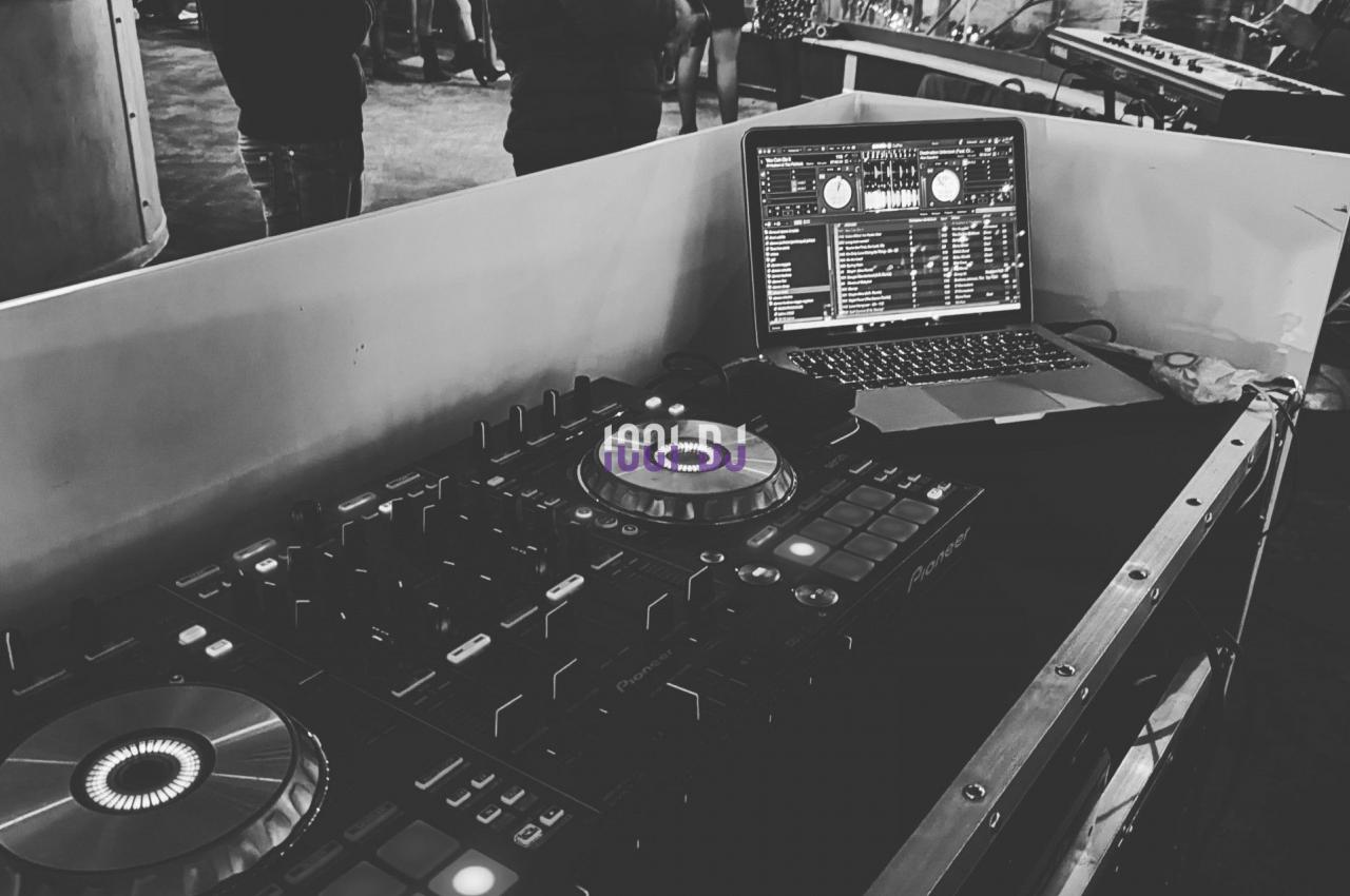 Console de DJ avec platines et ordinateur portable dans un espace animé, éclairé par des lumières urbaines.