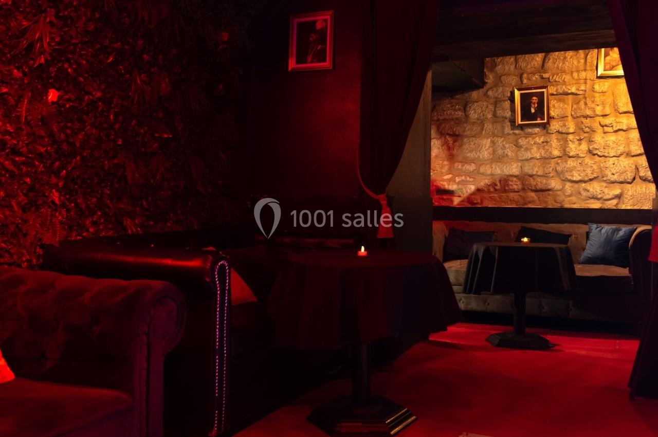 Salon intimiste avec éclairage rouge, canapés en cuir, tables basses et murs en pierre apparente.