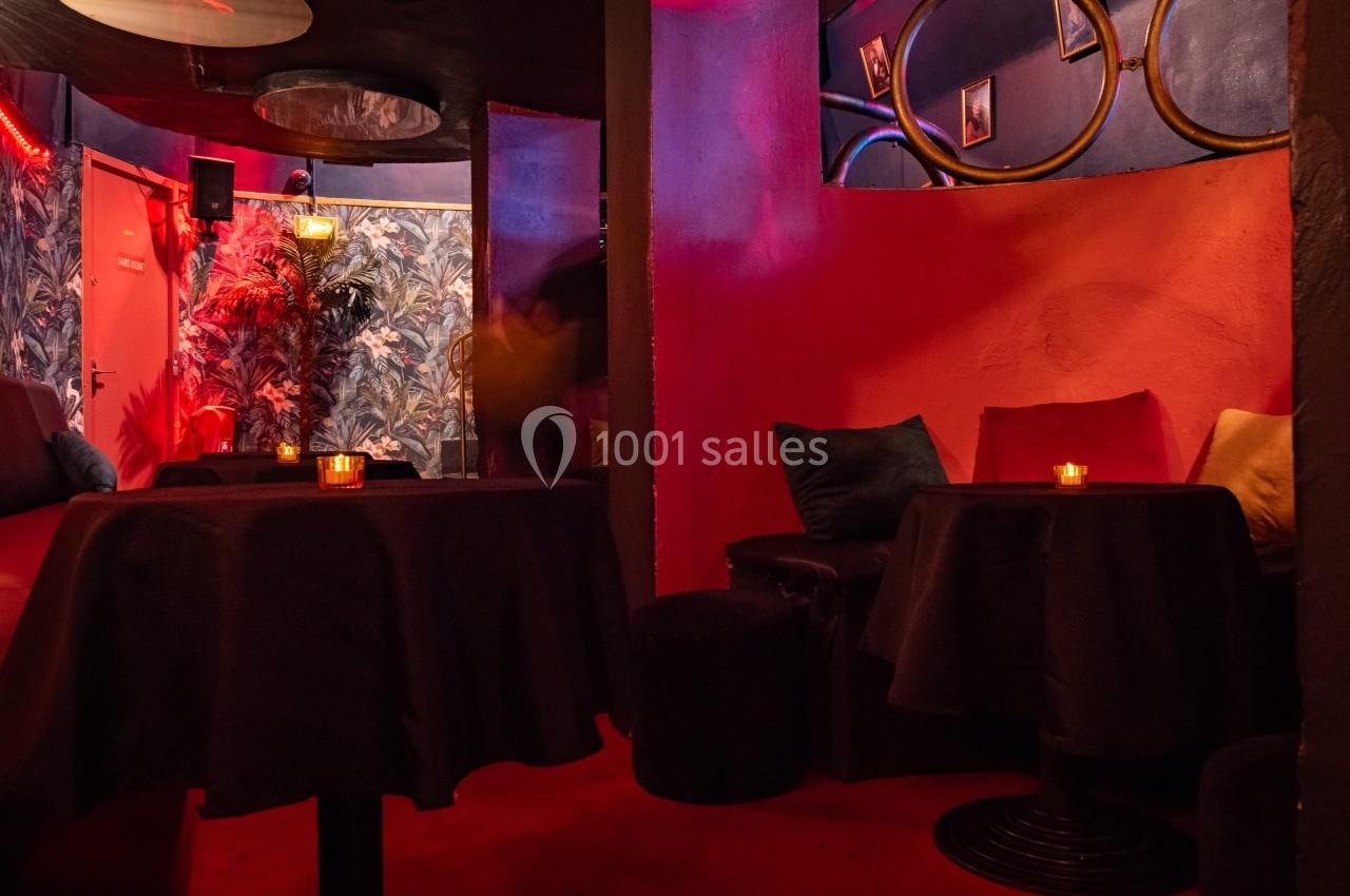 Salle tamisée avec tables rondes, bougies allumées, banquettes noires et murs décorés de motifs et cadres.