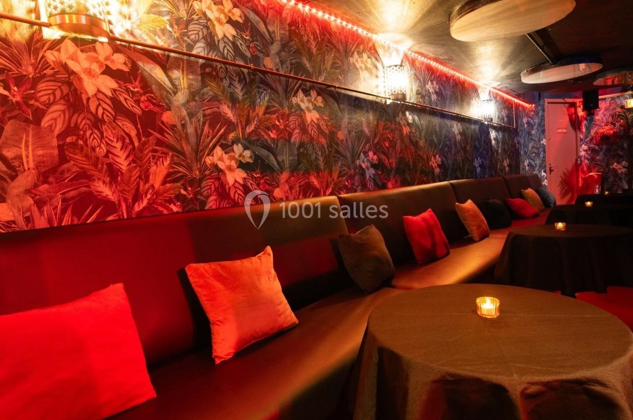 Banquettes noires avec coussins rouges et éclairage tamisé dans une pièce décorée de motifs tropicaux.