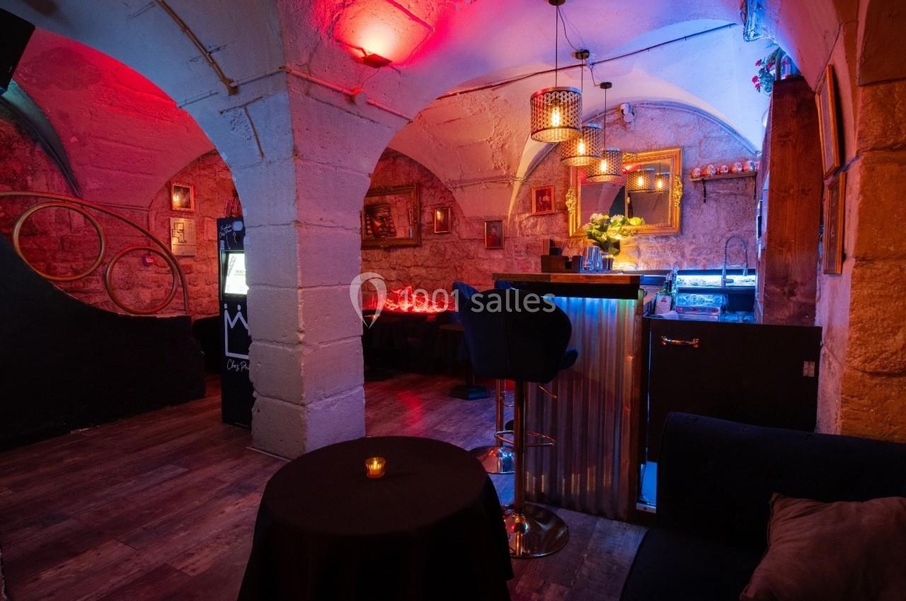 Intérieur d'un bar cosy avec éclairage tamisé, murs en pierre, tabourets et petite table avec bougie.
