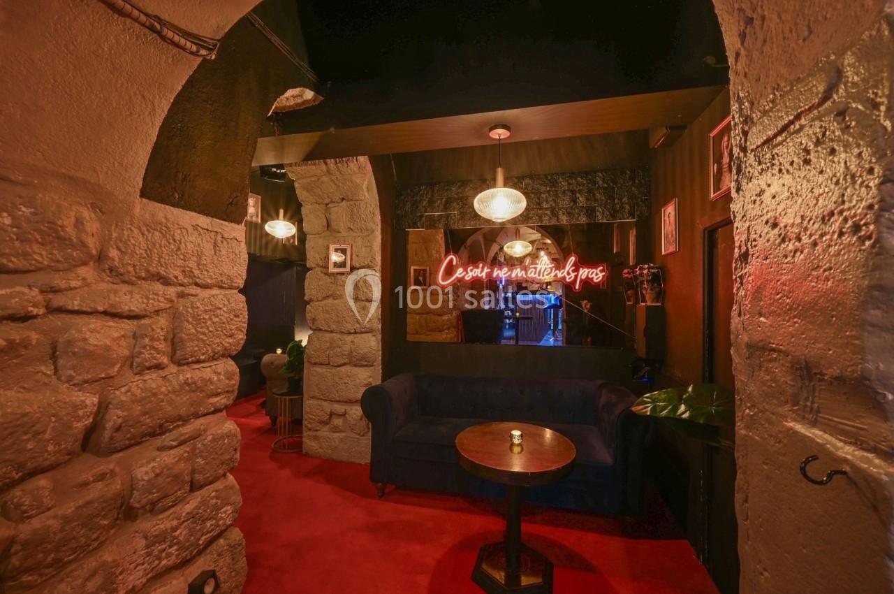 Salon cosy avec canapé bleu, table basse en bois, murs en pierre et néon rouge affichant un message lumineux.