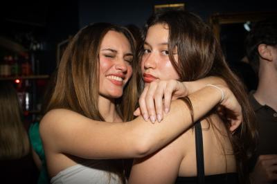 Deux femmes souriantes posent ensemble dans un environnement festif avec un éclairage tamisé.