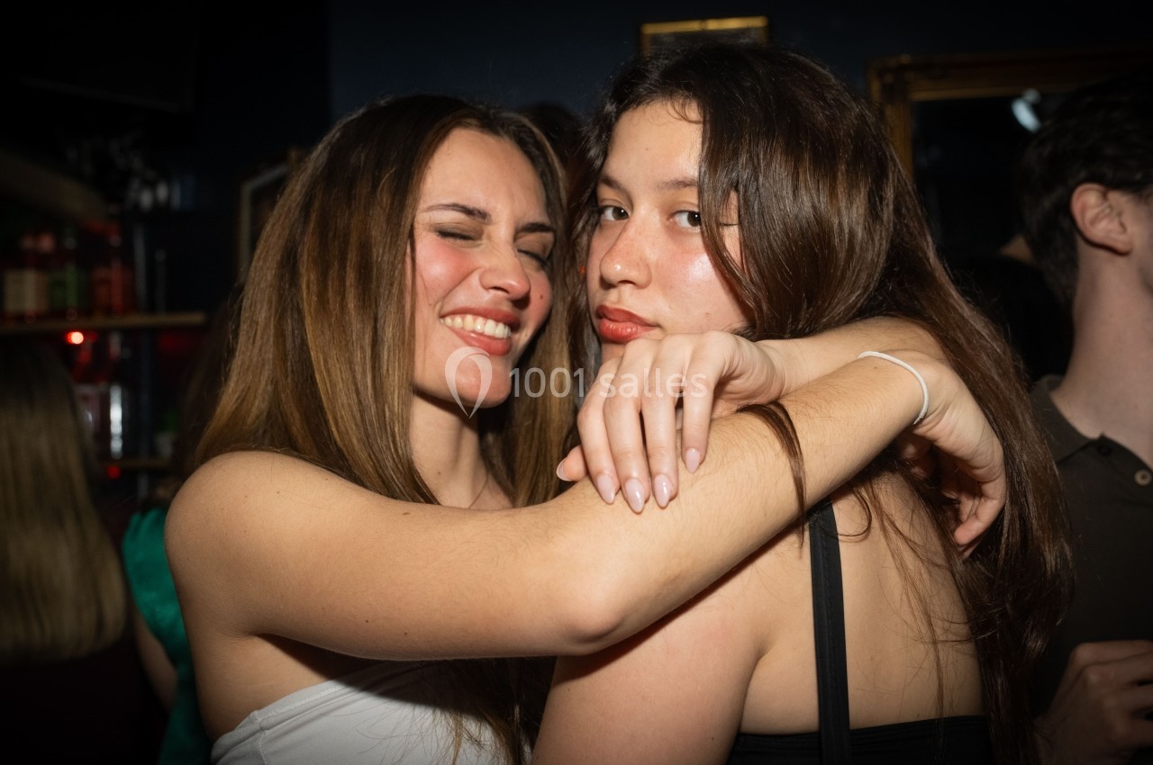 Deux femmes souriantes posent ensemble dans un environnement festif avec un éclairage tamisé.