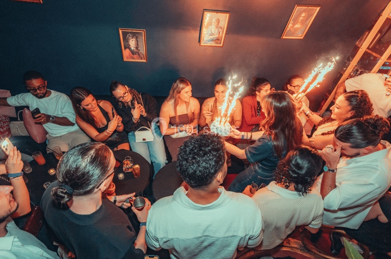 Groupe de personnes célébrant dans une pièce sombre, avec des étincelles et des boissons sur une table.
