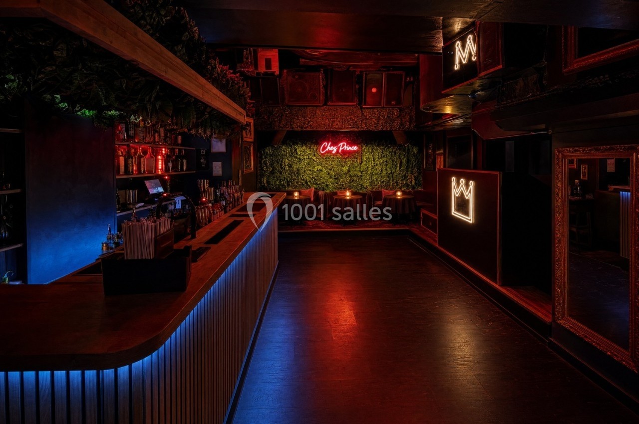 Intérieur d'un bar sombre avec un comptoir éclairé, des néons rouges et une décoration murale végétale.