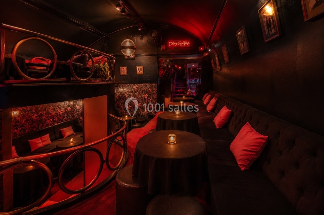 Salle intimiste avec éclairage tamisé, banquettes noires, coussins rouges et petites tables éclairées par des bougies.