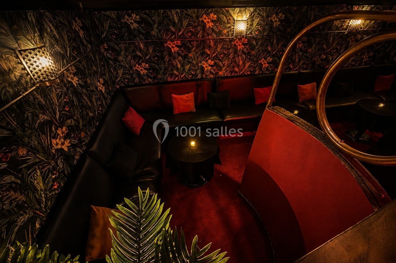 Banquette en cuir noir entourant des tables basses dans un espace sombre, décoré de motifs floraux et éclairé doucement.