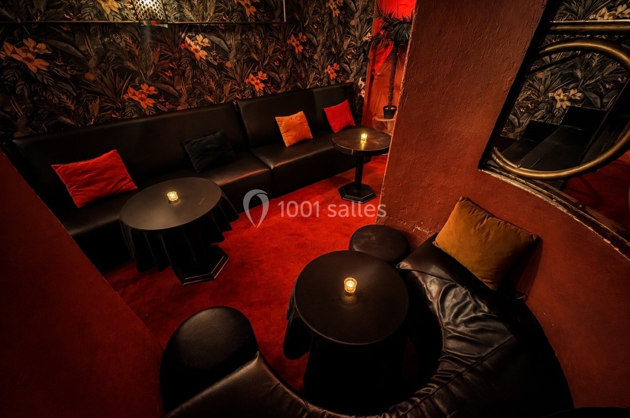 Salon intime avec canapés noirs, tables basses rondes, bougies allumées et murs ornés de motifs végétaux.
