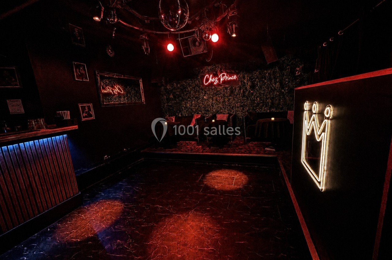 Salle sombre avec piste de danse, bar éclairé à gauche, néons rouges et logo lumineux en forme de couronne.