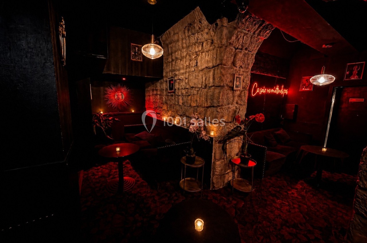 Salle sombre et intimiste avec murs en pierre, éclairage tamisé, bougies sur tables et néon rouge au mur.