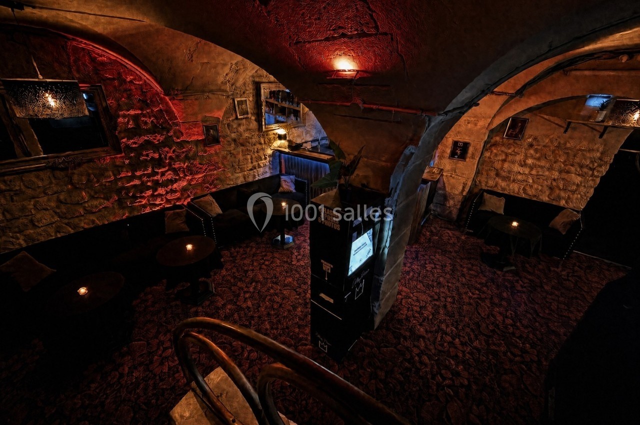 Salle voûtée en pierre avec éclairage tamisé, tables rondes et ambiance chaleureuse.