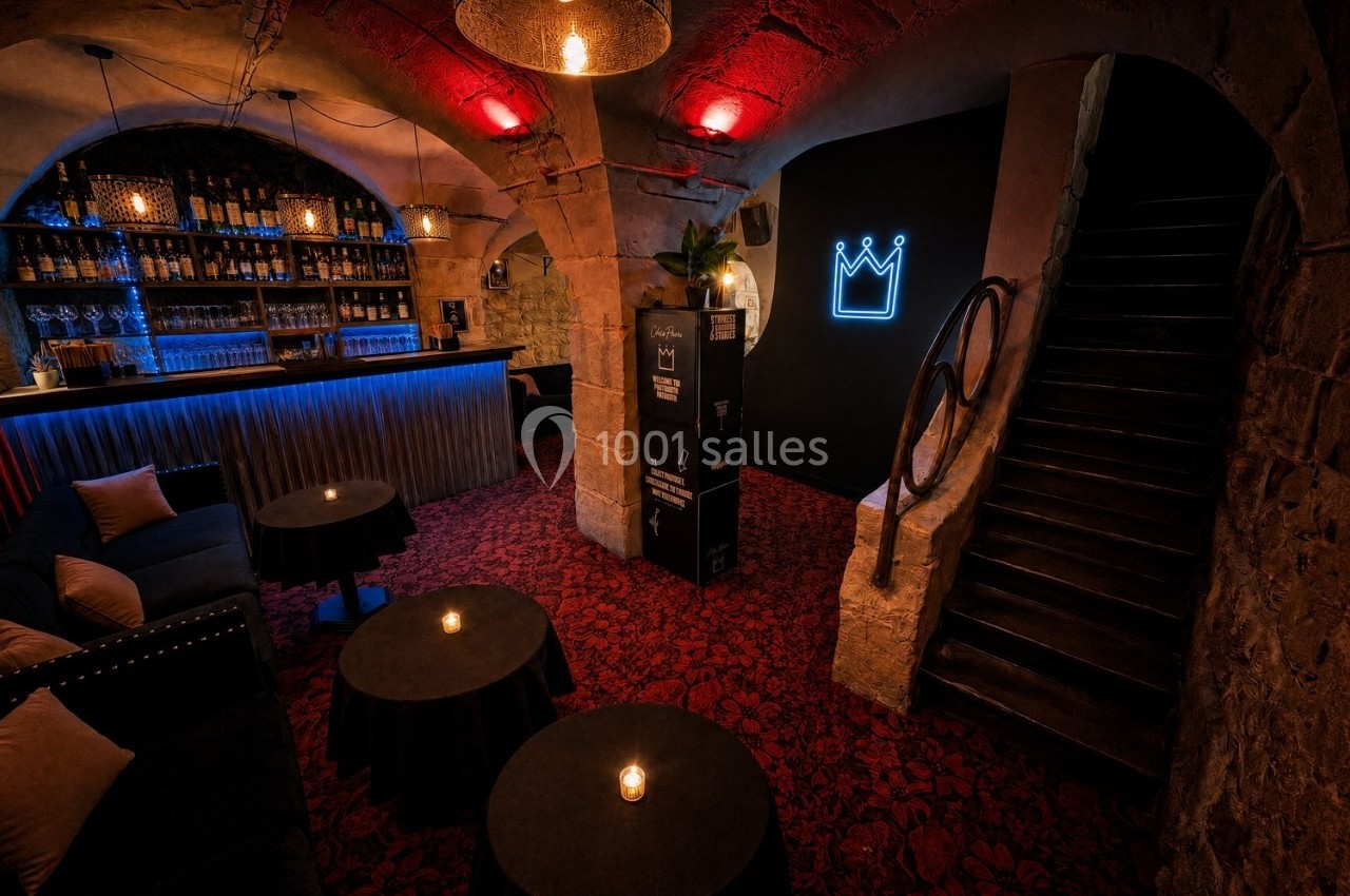 Salle voûtée avec bar éclairé, tables basses et fauteuils, éclairage tamisé et enseigne lumineuse en forme de couronne.