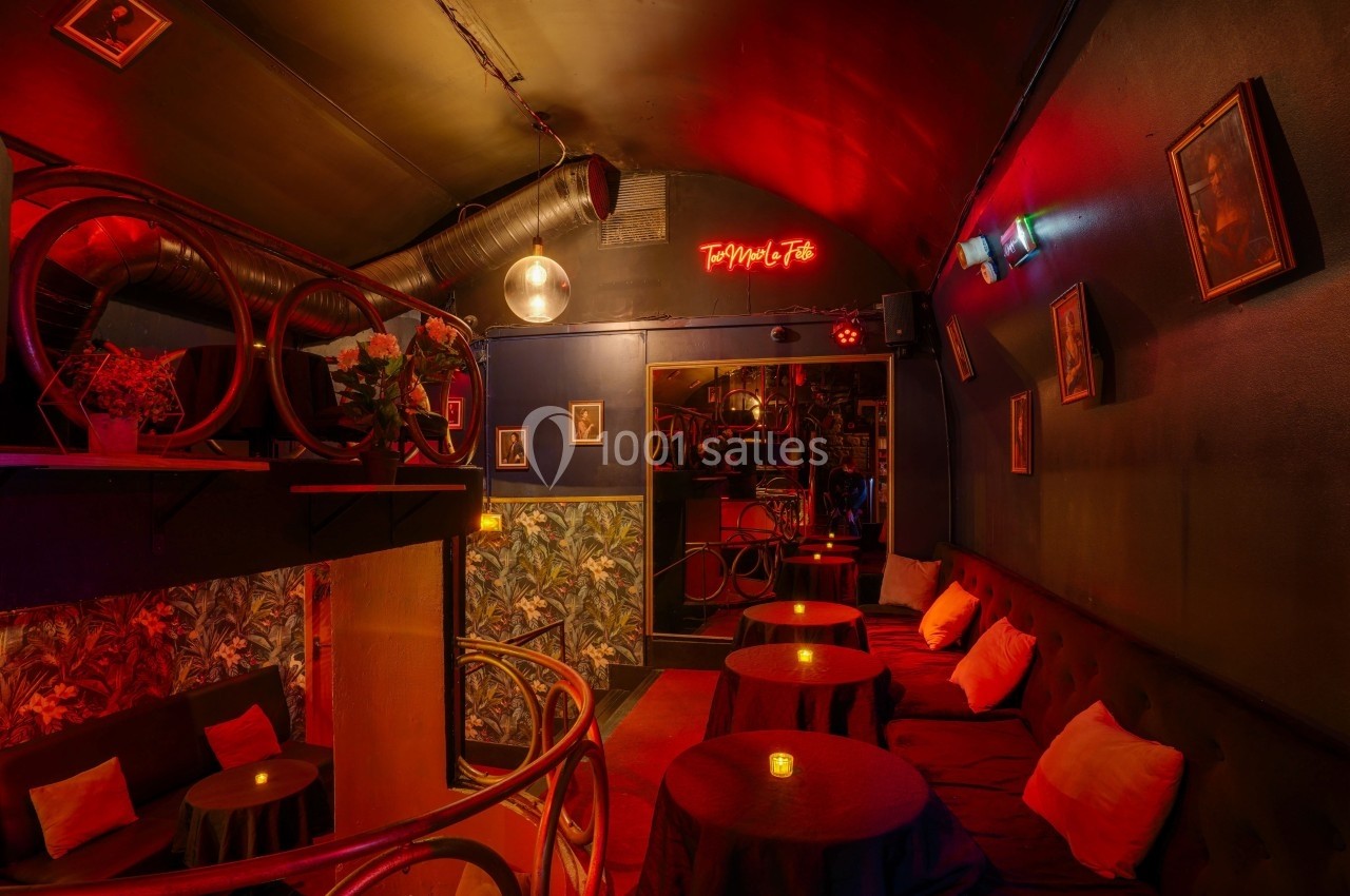 Intérieur d'un bar avec éclairage tamisé rouge, banquettes, petites tables avec bougies et décorations murales.