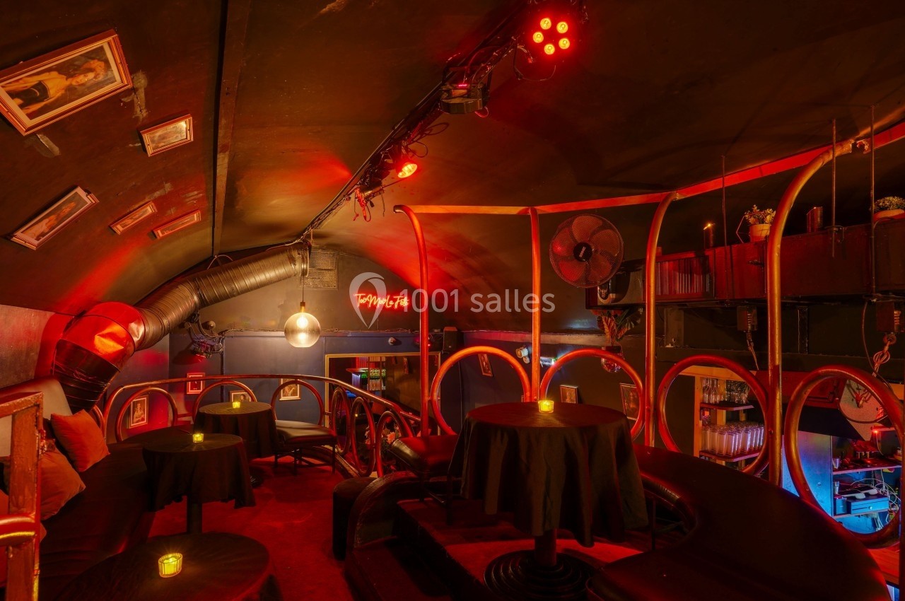 Salle intimiste avec tables rondes, éclairage rouge tamisé et décor rétro dans un espace voûté.