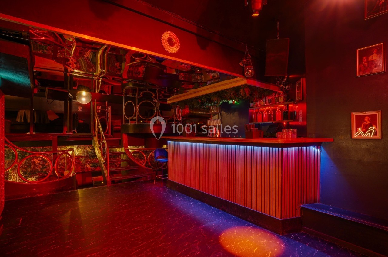 Intérieur d'un bar avec éclairage rouge et bleu, comptoir en bois, décorations murales et ambiance tamisée.