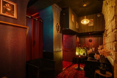 Couloir sombre avec murs noirs, tapis rouge à motifs, tableaux encadrés et petite table décorée de fleurs.