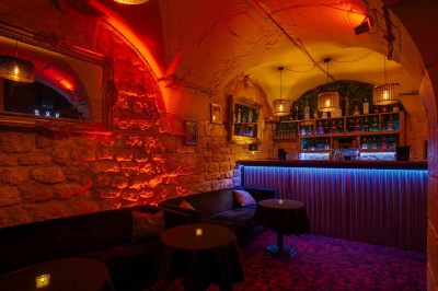 Couloir sombre avec murs noirs, tapis rouge à motifs, tableaux encadrés et petite table décorée de fleurs.