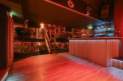 Salle sombre avec éclairage rouge, tables rondes, banquettes noires et décorations murales encadrées.