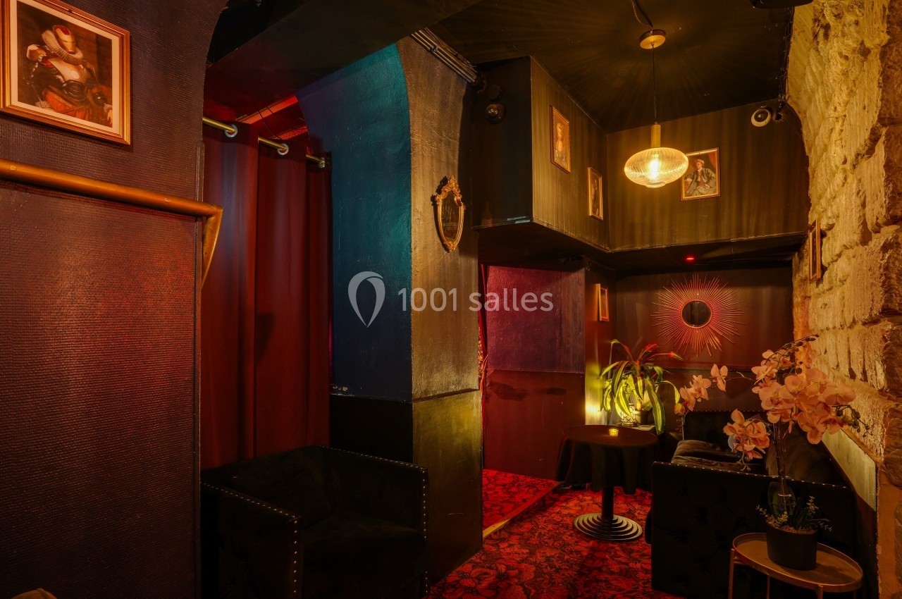 Salon intimiste avec fauteuils noirs, murs sombres, éclairage tamisé, décorations murales et plantes.