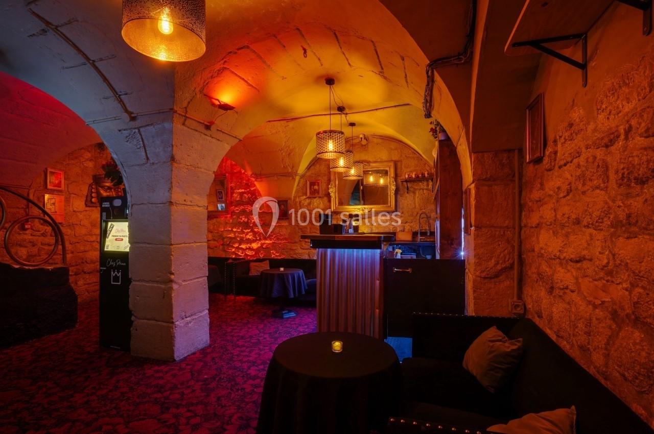 Salle voûtée avec éclairage tamisé, murs en pierre, tables basses et fauteuils disposés dans une ambiance chaleureuse.