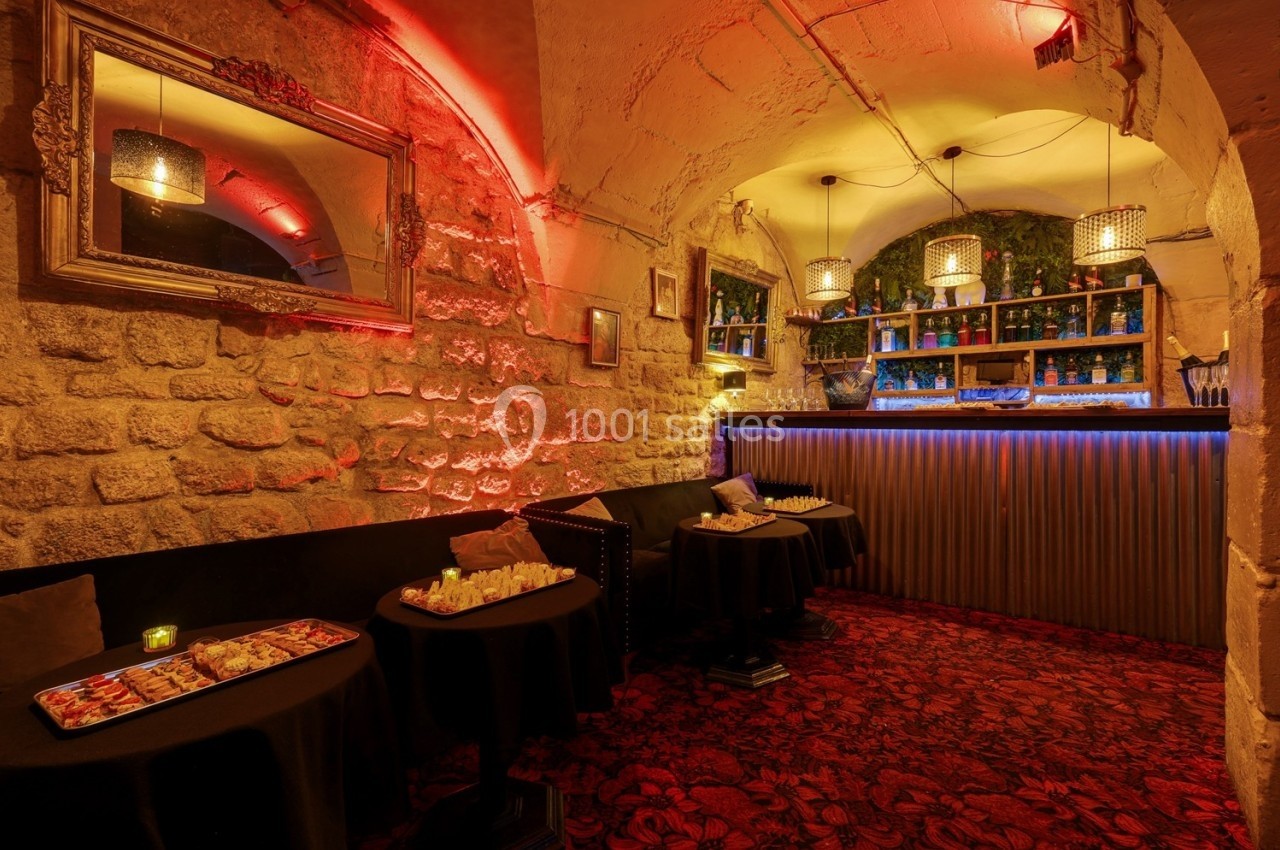 Salle voûtée avec murs en pierre, bar éclairé, tables dressées et ambiance tamisée chaleureuse.