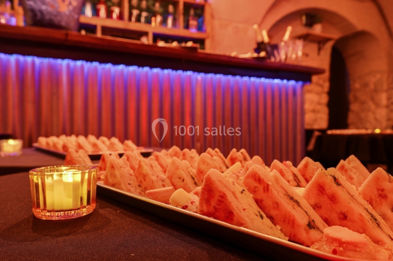 Plateaux de parts de focaccia disposés sur une table, avec un bar éclairé en arrière-plan dans une ambiance chaleureuse.