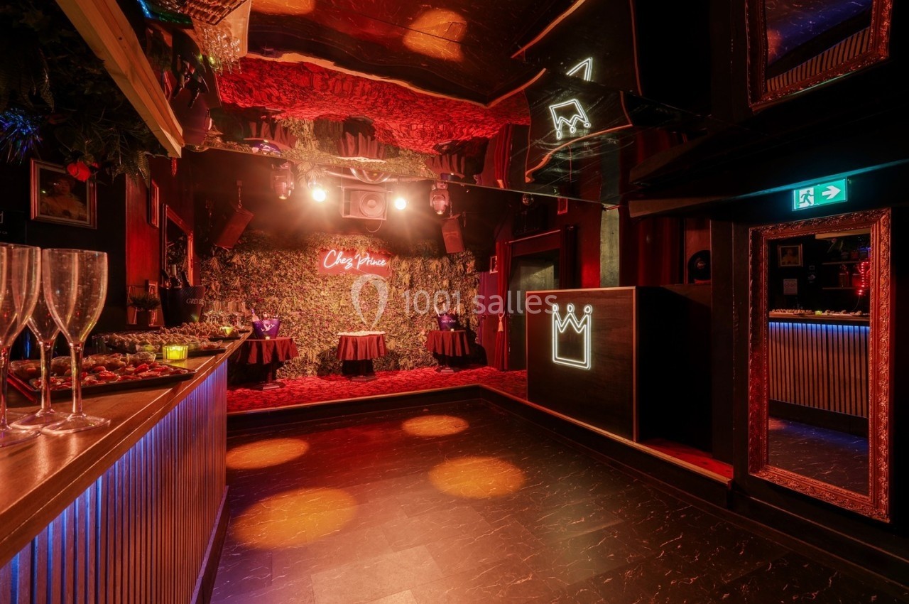 Salle de réception avec éclairage tamisé, bar à gauche, décoration végétale et enseigne lumineuse au fond.