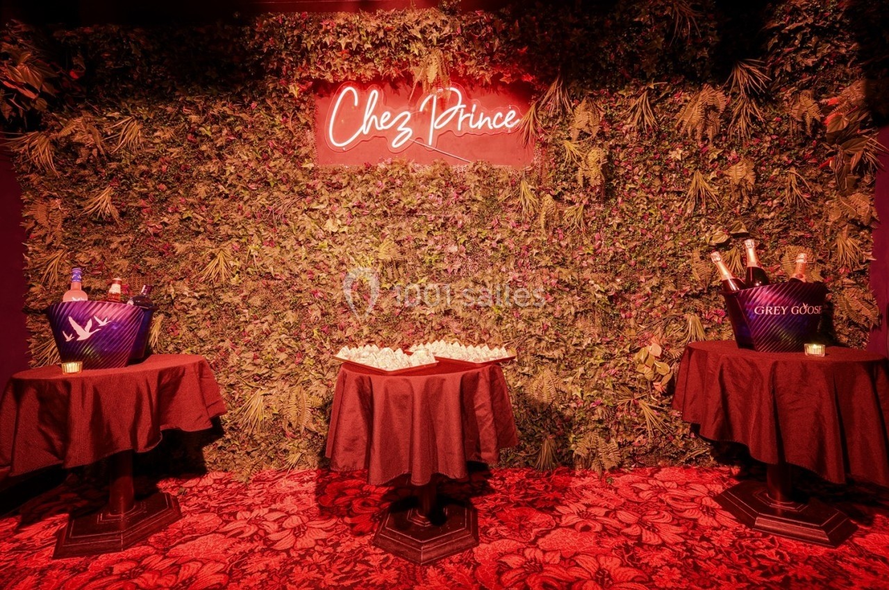 Mur végétal décoratif avec un néon ’Chez Prince’, entouré de tables avec seaux à champagne et tapis rouge au sol.
