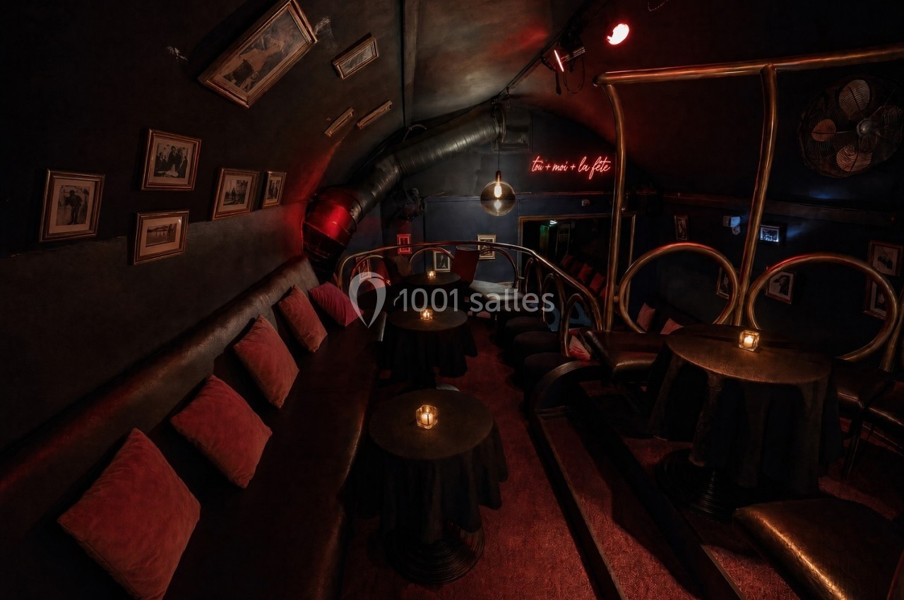 Salle sombre avec banquettes, petites tables éclairées par des bougies, décorations murales et lumière tamisée.