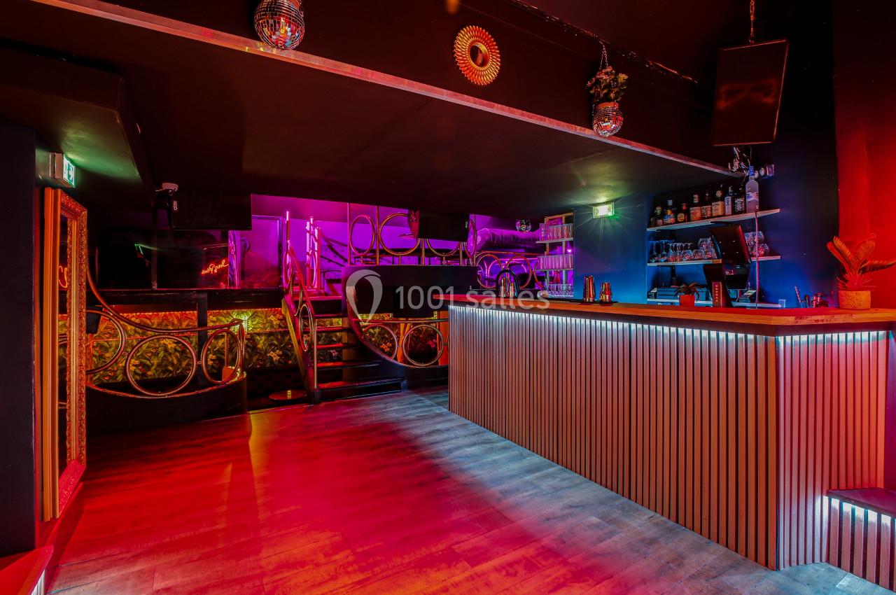 Intérieur d'un bar avec comptoir en bois, éclairage coloré et décorations murales dans une ambiance tamisée.