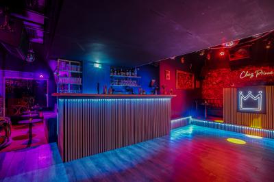 Salle sombre avec éclairage rouge, tables rondes, banquettes noires et décorations murales encadrées.