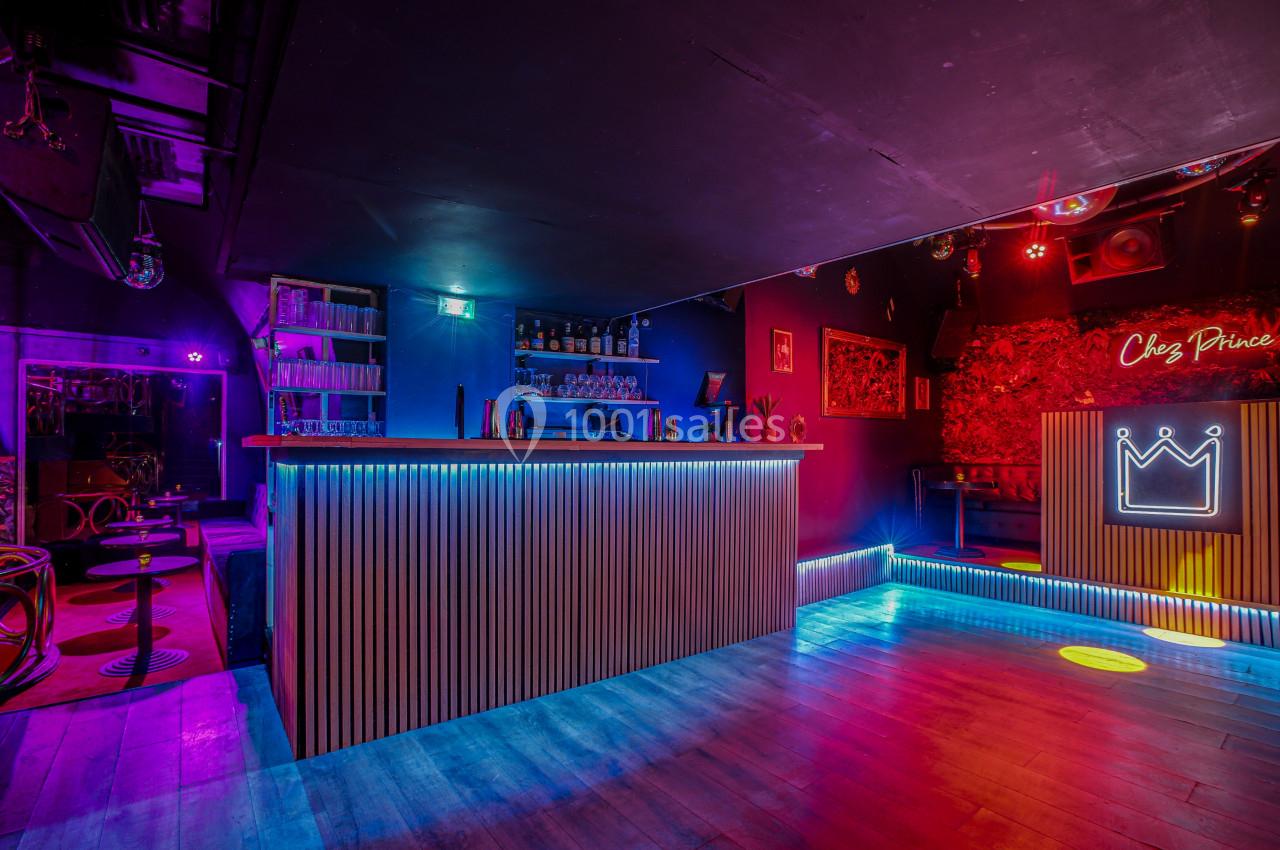 Bar coloré avec éclairage néon, comptoir en bois, étagères de bouteilles et espace de danse lumineux.