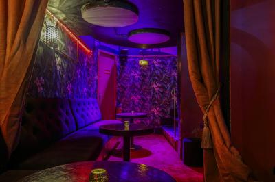 Salle sombre avec éclairage rouge, tables rondes, banquettes noires et décorations murales encadrées.
