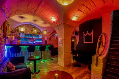 Salle sombre avec éclairage rouge, tables rondes, banquettes noires et décorations murales encadrées.