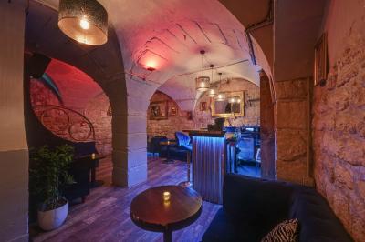 Salle sombre avec éclairage rouge, tables rondes, banquettes noires et décorations murales encadrées.