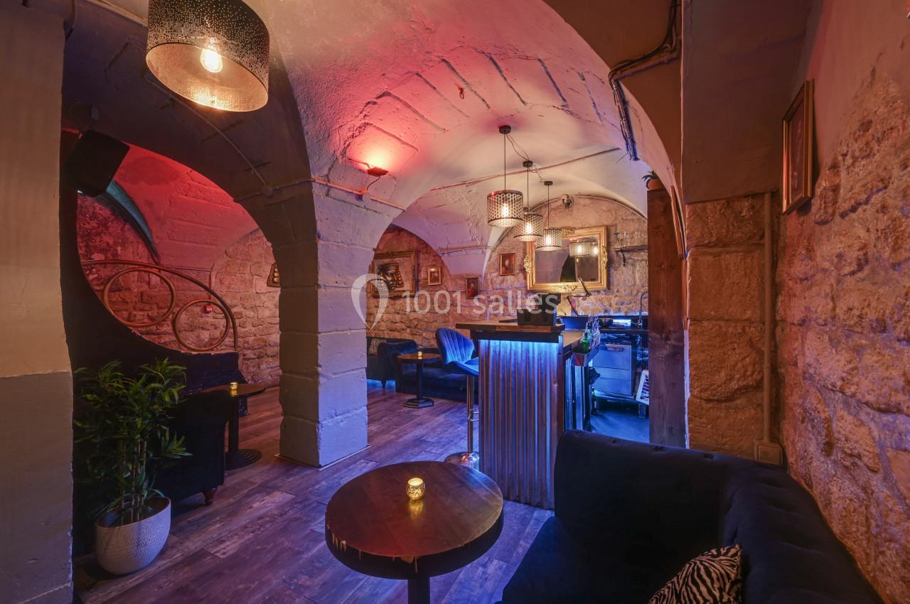 Intérieur d'un bar avec voûtes en pierre, éclairage tamisé, mobilier en bois et fauteuils, ambiance chaleureuse.