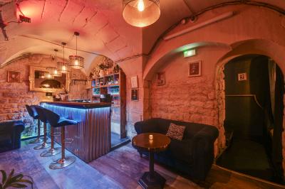 Salle sombre avec éclairage rouge, tables rondes, banquettes noires et décorations murales encadrées.