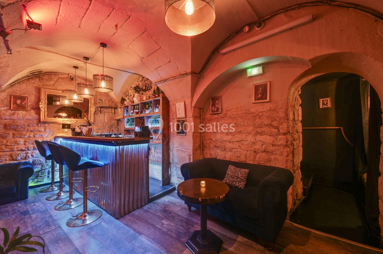 Bar intimiste avec comptoir éclairé, tabourets hauts, murs en pierre, canapés et éclairage tamisé.