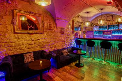 Salle sombre avec éclairage rouge, tables rondes, banquettes noires et décorations murales encadrées.