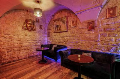 Salle sombre avec éclairage rouge, tables rondes, banquettes noires et décorations murales encadrées.