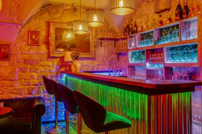 Salle sombre avec éclairage rouge, tables rondes, banquettes noires et décorations murales encadrées.