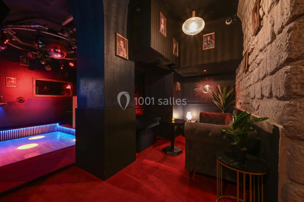 Espace intérieur avec fauteuils, murs en pierre et éclairage tamisé, donnant sur une petite piste de danse illuminée.