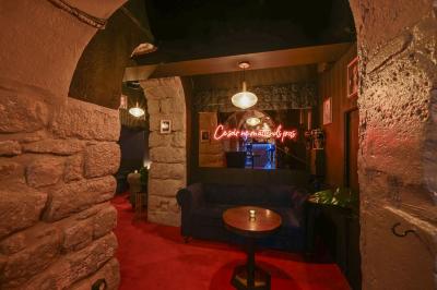 Salle sombre avec éclairage rouge, tables rondes, banquettes noires et décorations murales encadrées.