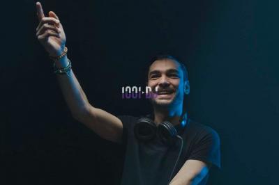 Portrait d'un homme souriant avec un éclairage tamisé sur fond sombre, un logo ’1001 DJ’ superposé au centre.